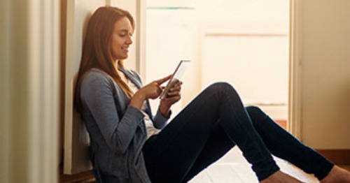 Young woman sitting on floor in house using tablet.